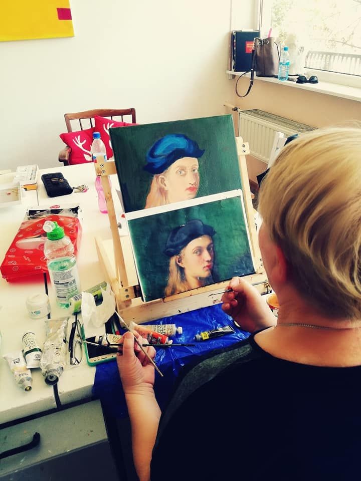 Person painting a portrait on a canvas in an art studio with various painting supplies on the table.